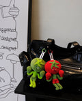 Wulibuddy Purr Red Boxing Tomato Buddy plush bag  Charm & keychain accessory two plush keychains shaped like a green tomato  and a red tomato on a black leather bag.