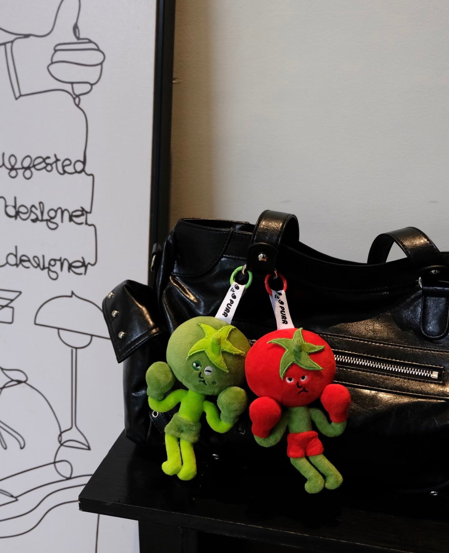 Wulibuddy Purr Red Boxing Tomato Buddy plush bag  Charm & keychain accessory two plush keychains shaped like a green tomato  and a red tomato on a black leather bag.
