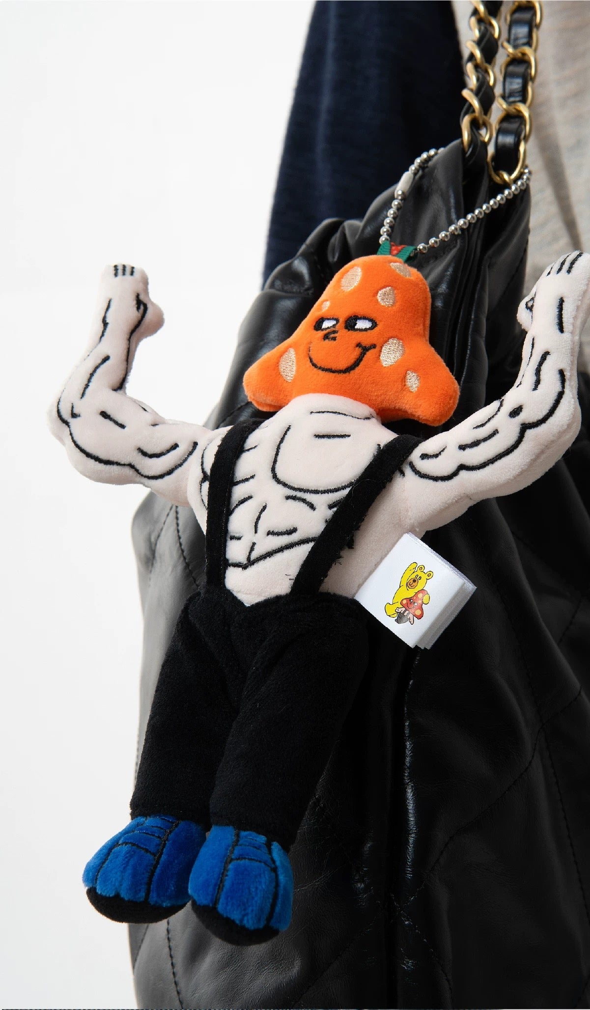 Muscle plush bag charm hanging on a black bag, WuliBuddy NYC character accessory