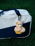 wulibuddy Coach Bear plush Bag Charm & keychain accessory attached to a white and navy bag on grass