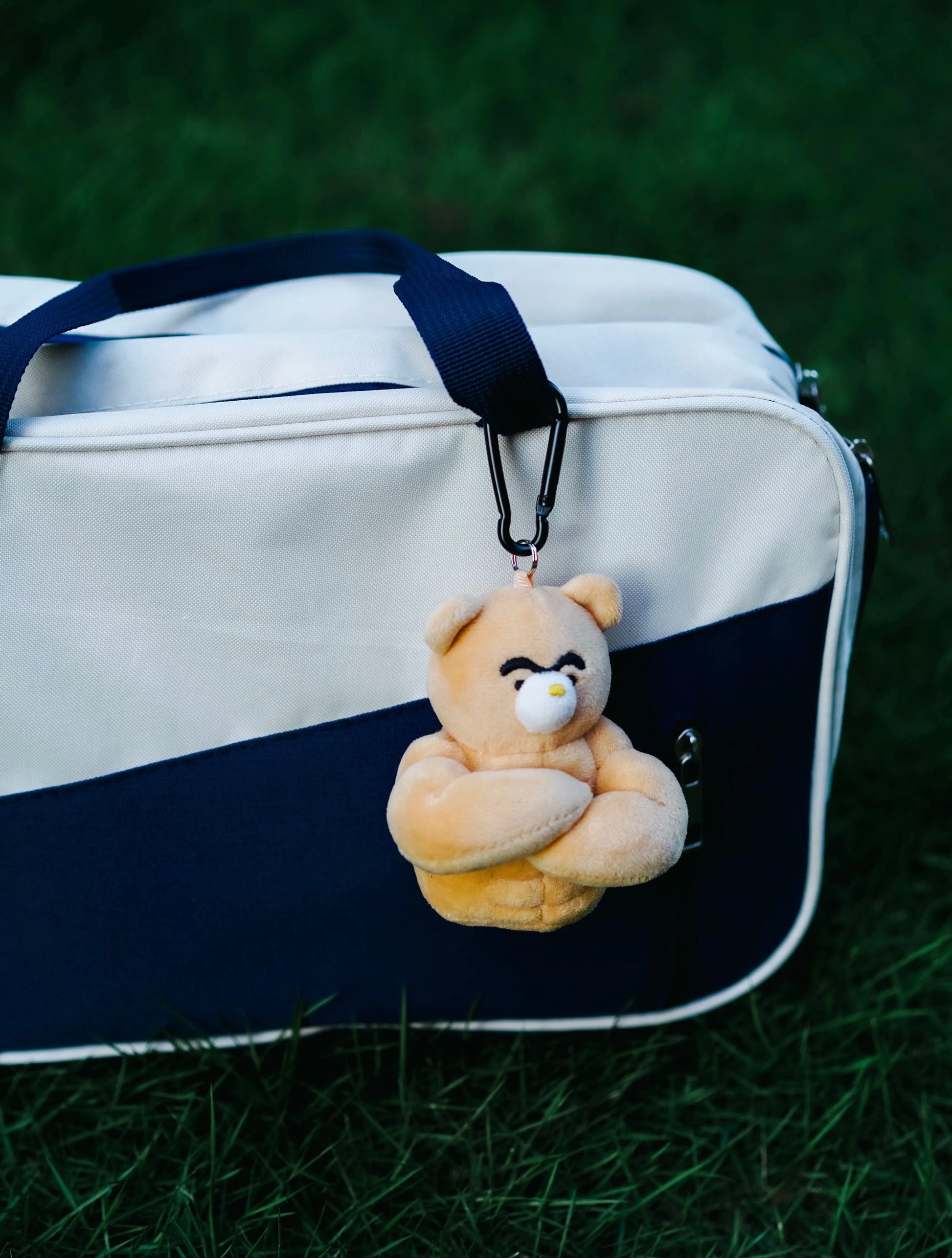 wulibuddy Coach Bear plush Bag Charm & keychain accessory attached to a white and navy bag on grass
